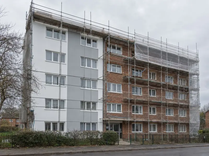 A five-storey block of flats half re-clad in white and grey insulated render, with scaffolding on the brick half