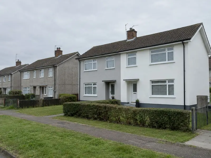 A pair of post-war concrete semi-detached houses newly rendered in white and grey beside neighbours still showing concrete panels